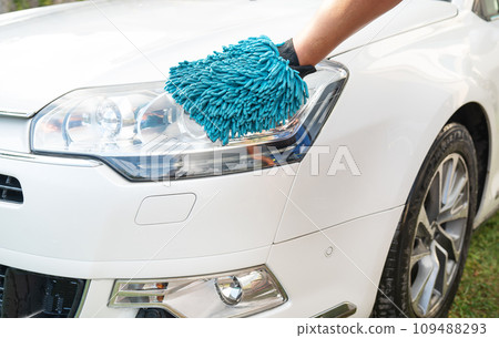 Hand in blue microfiber glove cleaning a white car s headlight. 109488293