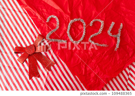 A red gift with a red bow and the numbers 2024 in silver glitter on a red and white striped background. The numbers 2024 are in silver glitter. A red gift with a red bow and the numbers 2024 in silver glitter on a red and white striped background. The numbers 2024 are in silver glitter. 109488365