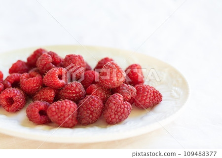 Fresh, ripe raspberries on a white plate, set against a white tablecloth. Perfect for a healthy snack or dessert. 109488377