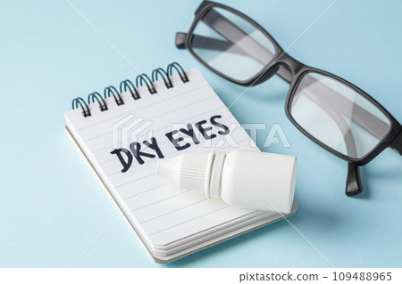 Dry eyes concept with eye drops and eyeglasses on blue background Dry eyes concept with eye drops and eyeglasses on blue background 109488965
