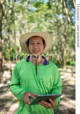 Asian young smart farmer smiles holding the tablet in the rubber plantation 109489211