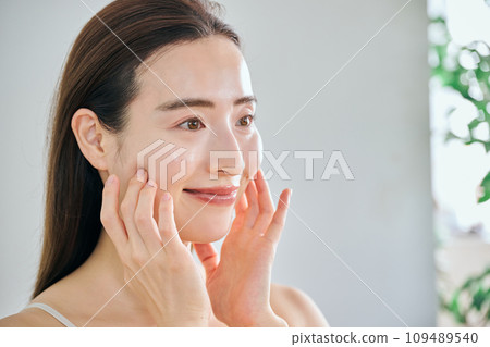 A woman in her 30s taking care of her skin by massaging her face A woman in her 30s taking care of her skin by massaging her face 109489540