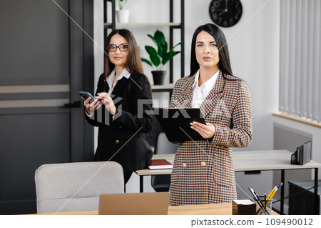 Two young attractive women are working in the office. A woman is talking on the phone, and her colleague is making notes in a notebook Two young attractive women are working in the office. A woman is talking on the phone, and her colleague is making notes in a notebook 109490012
