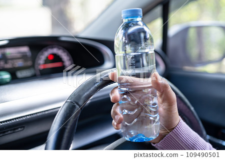 Asian woman driver holding bottle for drink water while driving a car. Plastic hot water bottle cause fire. Asian woman driver holding bottle for drink water while driving a car. Plastic hot water bottle cause fire. 109490501