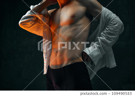 Cropped male body, muscular torso against dark textured studio background. Young man in white shirt and boxers 109490583