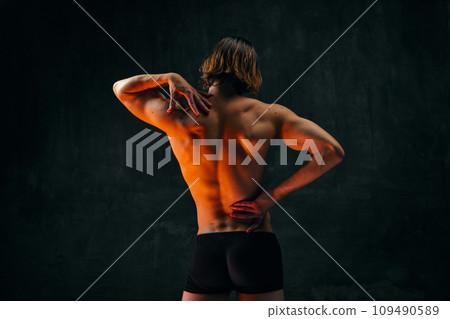 Healthy fit relief ack. Rear view of young shirtless man with muscular body standing in underwear against dark textured studio background 109490589