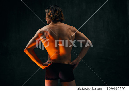 Healthy fit relief ack. Rear view of young shirtless man with muscular body standing in underwear against dark textured studio background Healthy fit relief ack. Rear view of young shirtless man with muscular body standing in underwear against dark textured studio background 109490591