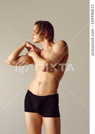 Handsome young man with fir, sportive muscular body posing in underwear shirtless against grey studio background Handsome young man with fir, sportive muscular body posing in underwear shirtless against grey studio background 109490615