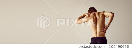 Muscular shirtless male body against grey studio background. Young man suffering from back and neck pains Muscular shirtless male body against grey studio background. Young man suffering from back and neck pains 109490626