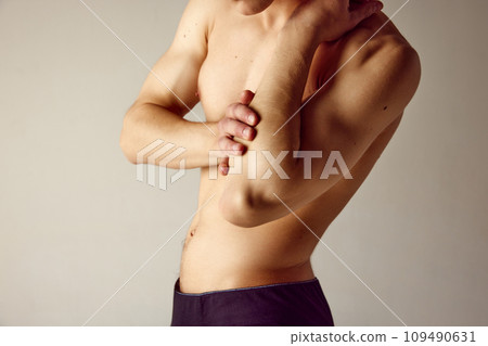 Cropped image of male shirtless body against grey studio background. Man holding elbow, suffering from pain. Inflammation 109490631