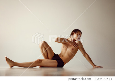 Young man with fit, healthy, muscular body sitting on floor in underwear against grey studio background Young man with fit, healthy, muscular body sitting on floor in underwear against grey studio background 109490645