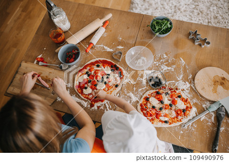 Daughter and mother making pizza together for dinner at the kitchen 109490976