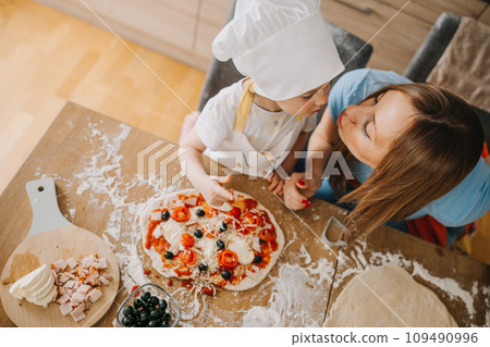 Daughter and mother making pizza together for dinner at the kitchen Daughter and mother making pizza together for dinner at the kitchen 109490996