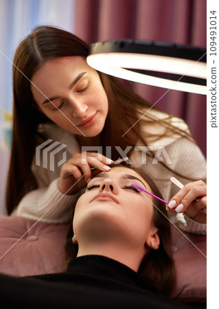 master using brush for combs the eyelashes of the client after the eyelash extension procedure. Cosmetology 109491014