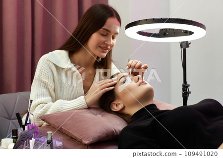cosmetologist removes glue cotton strip under eye. Eyelash extension procedure 109491020