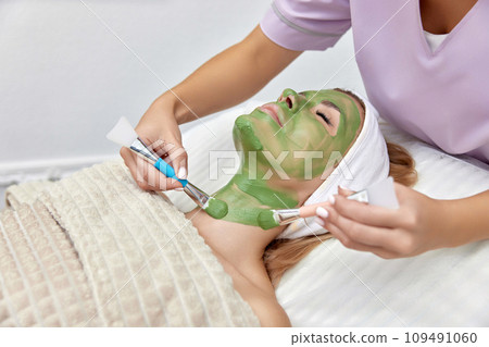 female beautician applies the mask to the face of beautiful woman in the spa salon. facial skin care 109491060