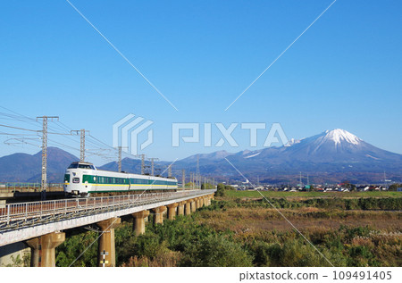 The reprinted green-colored 381 series limited express Yakumo runs over the long railway bridge of the Hino River with the snow-capped Mt. Mt. in the background. 109491405