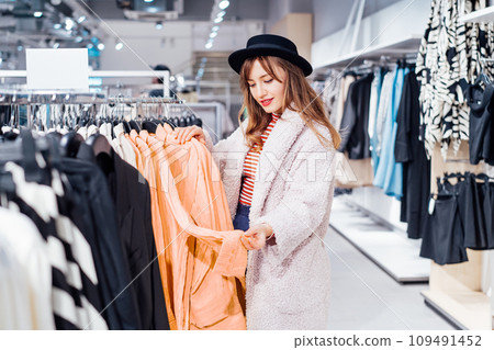 Fashion woman customer looking on peach color shirt in store. Buying clothes using fitting concept while choosing, professional stylist creating trendy look according to color of the 2024 year. Fashion woman customer looking on peach color shirt in store. Buying clothes using fitting concept while choosing, professional stylist creating trendy look according to color of the 2024 year. 109491452