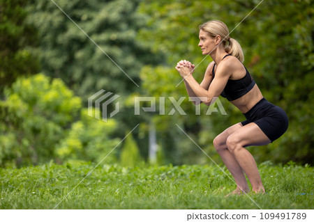 Beautiful woman working out doing squats in summer park. 109491789