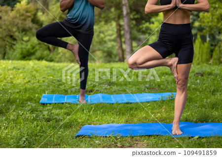 Unrecognizable man and woman doing yoga exercises in green park. Unrecognizable man and woman doing yoga exercises in green park. 109491859