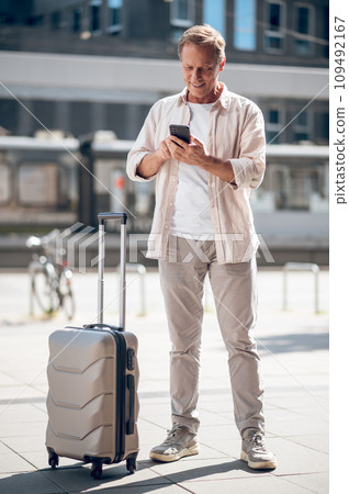 Handsome man with suitcase using smartphone browsing Internet on cellphone. 109492167