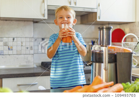 Little boy drinking freshly squeezed carrot juice from a glass in the kitchen Little boy drinking freshly squeezed carrot juice from a glass in the kitchen 109493703
