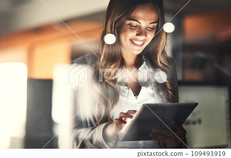 Working late, overtime and dedication with a happy, positive and motivated business woman working on a tablet in her office. Young female executive smiling while feeling dedicated and determined 109493919