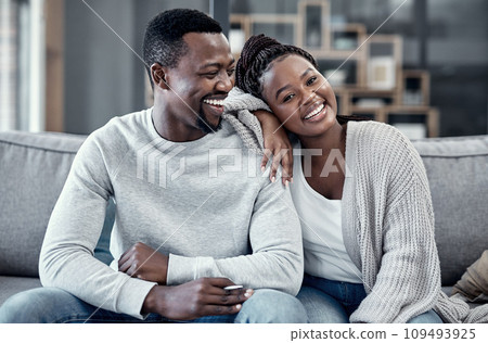 Happy, in love, and carefree couple relaxing, smiling and laughing together at home portrait while enjoying their weekend spent indoors. Young African wife and loving husband bonding on their couch 109493925