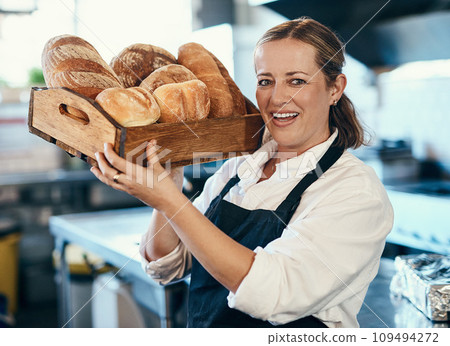 Baker, pastry chef and cafe owner carrying a tray of fresh rolls and bread loaf assortment in a coffee shop. Portrait of a small business entrepreneur in an apron with freshly made consumables Baker, pastry chef and cafe owner carrying a tray of fresh rolls and bread loaf assortment in a coffee shop. Portrait of a small business entrepreneur in an apron with freshly made consumables 109494272