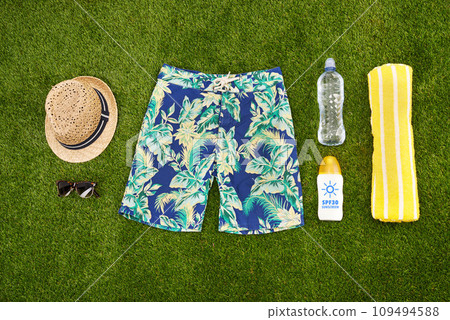 Mens casual summer fashion with accessories items, overhead top view. Marketing or advertising beach or pool swim clothes and equipment for men on fresh cut grass or astro turf over copy space. Mens casual summer fashion with accessories items, overhead top view. Marketing or advertising beach or pool swim clothes and equipment for men on fresh cut grass or astro turf over copy space. 109494588