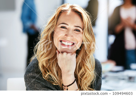 A female leader, successful and ambitious startup CEO smiling and sitting in a modern office. Happy, confident and attractive business female with her colleagues in the background. 109494603
