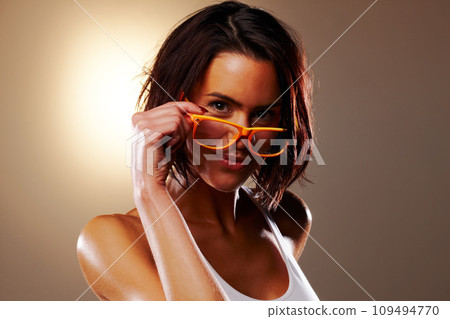 Portrait, fashion and glasses with a young woman in studio on a gray background for vision or style. Trendy, eyewear and a confident model flirting while peeking over prescription frame lenses Portrait, fashion and glasses with a young woman in studio on a gray background for vision or style. Trendy, eyewear and a confident model flirting while peeking over prescription frame lenses 109494770