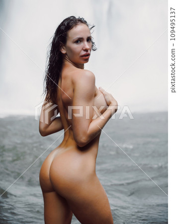 Naked woman staying near waterfall. Traveler nudist girl posing on waterfall with powerfull stream Naked woman staying near waterfall. Traveler nudist girl posing on waterfall with powerfull stream 109495137