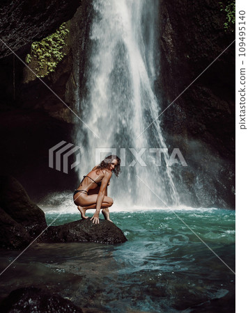 Woman in bikini enjoying near waterfall. Traveler young girl posing on waterfall Woman in bikini enjoying near waterfall. Traveler young girl posing on waterfall 109495140