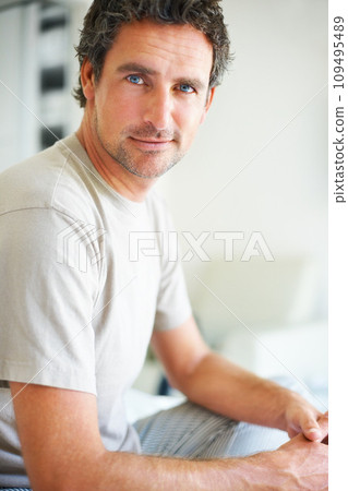 Portrait, relax and a mature man in the bedroom of his home to relax on a morning of the weekend. Face, wellness and happy with a confident person in casual pajamas sitting on a bed in his apartment 109495489