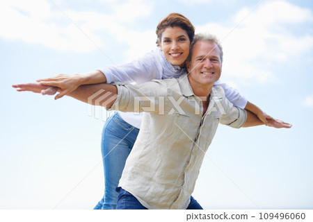 Mature couple, portrait and piggy back on vacation, airplane hands and happiness in blue skies. Man, woman and bonding together with smile, marriage and commitment with affection, holiday and joyful Mature couple, portrait and piggy back on vacation, airplane hands and happiness in blue skies. Man, woman and bonding together with smile, marriage and commitment with affection, holiday and joyful 109496060