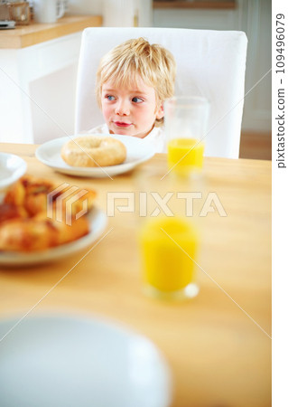 Kid, breakfast and bagel at home in the morning with food, smile and happy from eating. Family, dinner table and hungry young child with meal for health and nutrition in a house with orange juice 109496079