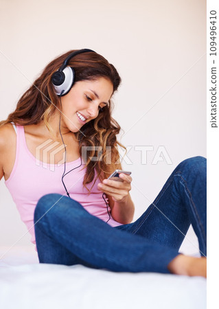 Smile, headphones and young woman in bedroom listening to music, playlist or radio at home. Happy, technology and face of female person from Canada relax on bed and stream song or album in apartment 109496410