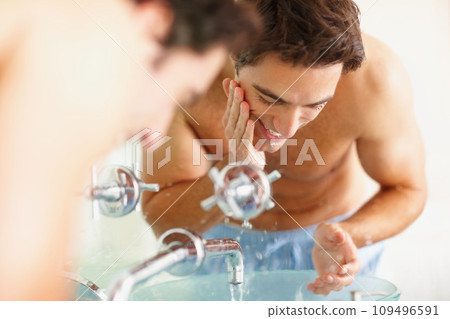 Man, face and smile with water, cleaning and skincare in bathroom for grooming, wellness and health. Happy person, hand and basin with soap for facial hygiene, morning routine or bacteria in home 109496591