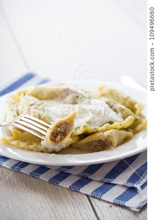 cooked dumplings with meat, spices and sour cream, in a plate on a light wooden table. 109496660