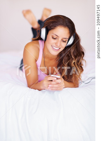 Smile, headphones and young woman on bed listening to music, playlist or radio at home. Happy, technology and female person from Canada relax and streaming song or album in bedroom at her apartment. Smile, headphones and young woman on bed listening to music, playlist or radio at home. Happy, technology and female person from Canada relax and streaming song or album in bedroom at her apartment. 109497145