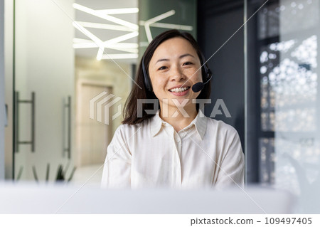 Portrait of online support worker, asian woman with headset phone smiling and looking at camera, businesswoman working in laptop at workplace inside office, call center call center support service. 109497405