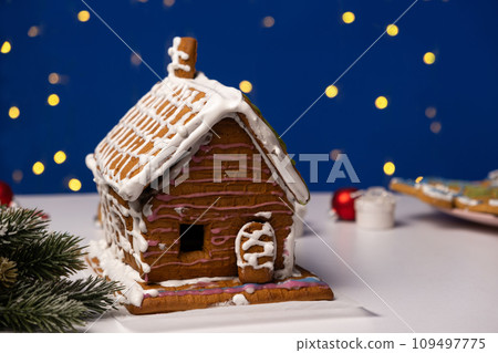 Christmas house made of gingerbread cookies decorated with sugar icing on blue background with bokeh garland 109497775