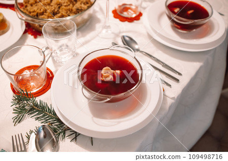 Christmas beetroot soup, borscht with small dumplings with mushroom filling in a ceramic bowl on a table. Traditional Christmas eve dish in Poland. Christmas beetroot soup, borscht with small dumplings with mushroom filling in a ceramic bowl on a table. Traditional Christmas eve dish in Poland. 109498716