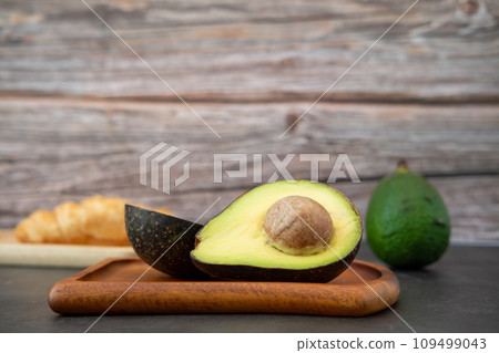 halved avocado on wooden plate and croissant on a black background halved avocado on wooden plate and croissant on a black background 109499043