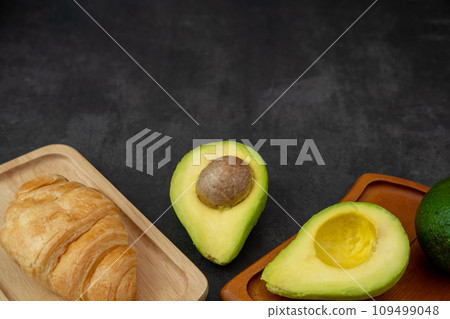 Top view of halved avocado on plate and croissant on a black background Top view of halved avocado on plate and croissant on a black background 109499048
