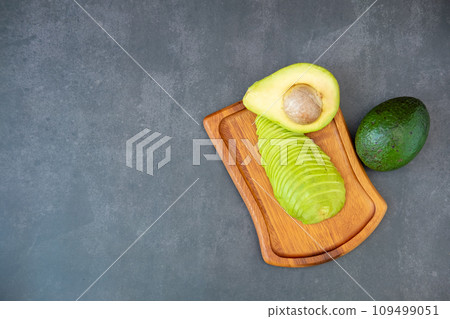 Top view of halved and finely sliced avocado on wooden plate on black background. 109499051