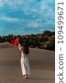 A beautiful dark-haired woman holds a Turkish flag in her hands, rear view. A woman is traveling in Turkey. A tourist on the background of Patara beach in Turkey. Vacation in Turkey. Turkish flag 109499671