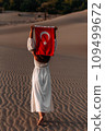 A beautiful dark-haired woman holds a Turkish flag in her hands, rear view. A woman is traveling in Turkey. A tourist on the background of Patara beach in Turkey. Vacation in Turkey. Turkish flag 109499672