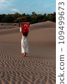 A beautiful dark-haired woman holds a Turkish flag in her hands, rear view. A woman is traveling in Turkey. A tourist on the background of Patara beach in Turkey. Vacation in Turkey. Turkish flag 109499673